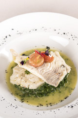 Perch fillet with spinach, sauce and tomato, decorated with eatable flowers and red leafs, placed on white plate, light background, isolated