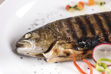 Grilled trout, served with lemon and decorated with radish and fresh leafs, light background, isolated