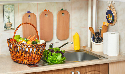 vegetables and fresh greens in basket in kitchen interior, healthy food concept