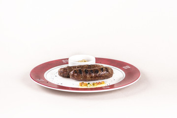 Homemade sausages, served with mustard and decorated with herbs, isolated on light background, white plate