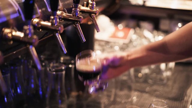 Close up of an unrecognizable young bartender pouring beer into a glass and putting it on a tray. He is ready to deliver. Handheld real time close up shot