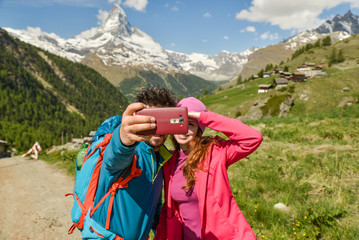 A couple hikers Hiking with backpacks walk along a beautiful mountain area. Taking a selfie. Holding the phone. The concept of active rest. Switzerland 2017