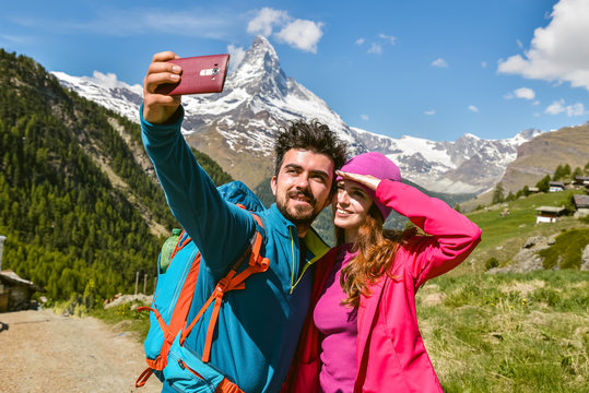A couple hikers Hiking with backpacks walk along a beautiful mountain area. Taking a selfie. Holding the phone. The concept of active rest. Switzerland 2017