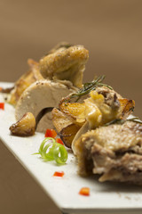 Roasted cock with potatoes, with green herbs, placed on a white plate, brown background