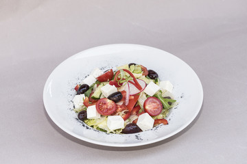 Fresh greek salad, decorated with herbs, isolated on light background, white plate