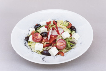 Fresh greek salad, decorated with herbs, isolated on light background, white plate