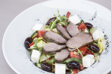Fresh greek salad and smoked pork tenderloin, decorated with herbs, isolated on light background, white plate