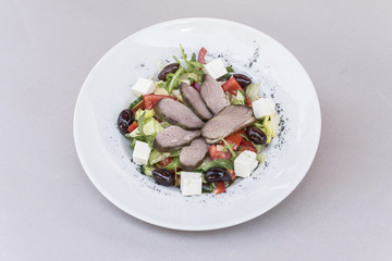 Fresh greek salad and smoked pork tenderloin, decorated with herbs, isolated on light background, white plate