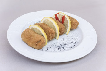 Fried pane sweetbreads, served with slices of lemon, decorated with herbs, isolated on light background, white plate