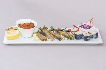 Plate with various types of fish, smoked and marinated, served with fresh salad, vegetable salad, onion salad, decorated with herbs, isolated on light background, white plate