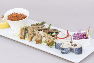 Plate with various types of fish, smoked and marinated, served with fresh salad, vegetable salad, onion salad, decorated with herbs, isolated on light background, white plate
