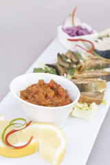 Plate with various types of fish, smoked and marinated, served with fresh salad, vegetable salad, onion salad, decorated with herbs, isolated on light background, white plate