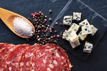 Roquefort slices on a board with peppercorns, salami slices and salt on a spoon on a background - 159773451