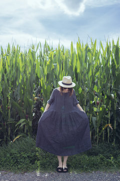femme en robe avec chapeau devant un champs de bl&eacute; vert