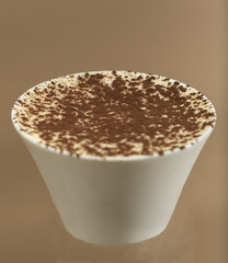 Traditional Italian dessert tiramisu in a white cup, brown background