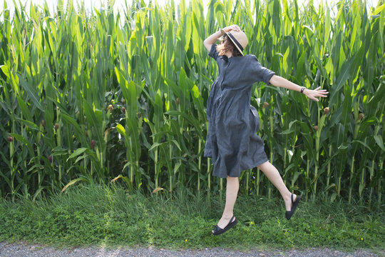 femme qui saute avec un chapeau devant un champs de bl&eacute;