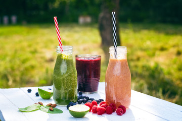     Blueberry, spinachy and orange smoothie on a wooden white background in nature. Glasses of smoothie with berry and mint. Berry, leaf and lime, raspberries on a table. Fruit Healthy food. 