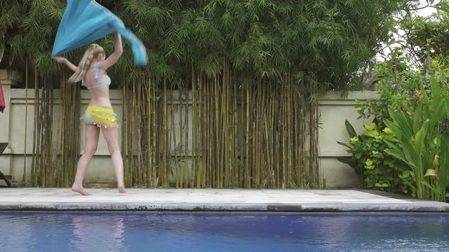 young slender woman dances an oriental dance near pool in tropical resort