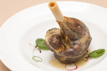 Roasted lamb leg, served with white sauce, decorated with herbs, placed on white plate, light background, isolated