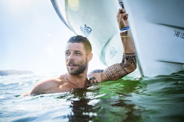 Man in ocean hanging off boat.