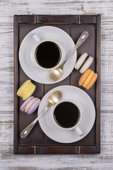 Two cups of coffee, spoon and macaron cakes on tray on white wooden table. Lifestyle concept. Top view