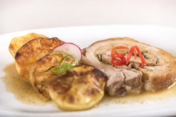 Slice roasted pork, served with potatoes and decorated with herbs, placed on white plate, light background, isolated