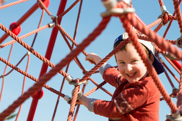 Young boy child playing at outdoor playground climbing net