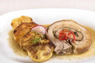 Slice roasted pork, served with potatoes and decorated with herbs, placed on white plate, light background, isolated