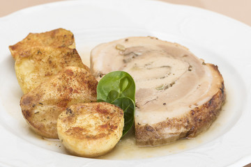 Slice roasted pork, served with potatoes and decorated with herbs, placed on white plate, light background, isolated