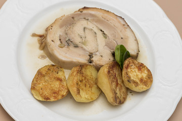 Slice roasted pork, served with potatoes and decorated with herbs, placed on white plate, light background, isolated