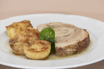 Slice roasted pork, served with potatoes and decorated with herbs, placed on white plate, light background, isolated