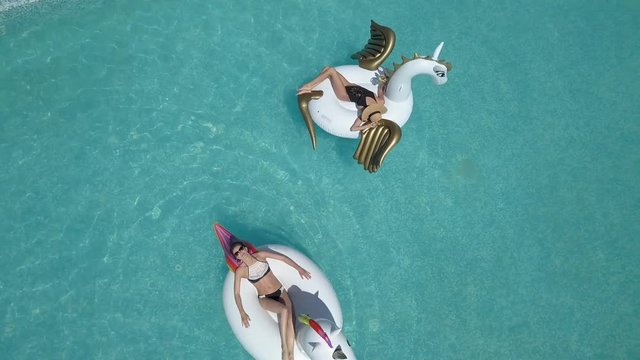 Aerial - Beautiful girls in a bikini on an inflatable pegasus and unicorn mattress in the pool. Young woman enjoys a sunny afternoon with a cocktail in hands. Shooting with quadrocopter