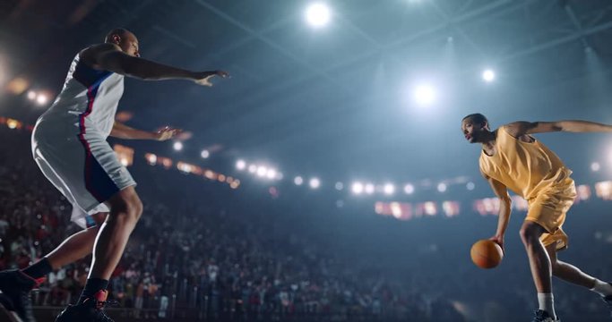 4K footage in slow motion basketball player dribbling in front of rival player. The action takes place in 3d made basketball arena full of spectators. All players wear unbranded basketball uniform.
