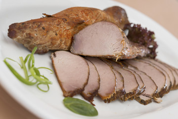 Pork tenderloin, decorated with green and red leafs, placed on a white and red plate, light background