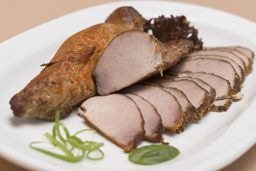 Pork tenderloin, decorated with green and red leafs, placed on a white and red plate, light background