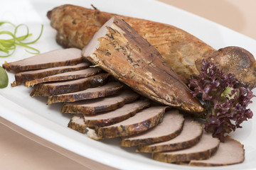 Pork tenderloin, decorated with green and red leafs, placed on a white and red plate, light background