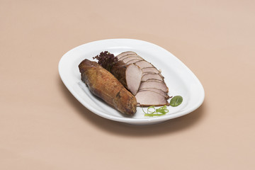 Pork tenderloin, decorated with green and red leafs, placed on a white and red plate, light background