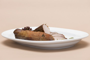 Pork tenderloin, decorated with green and red leafs, placed on a white and red plate, light background