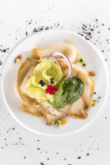 Fresh appetizer with smoked white fish, rucola, baby spinach and green salad, with red eatable flowers, placed on white plate, light background, isolated