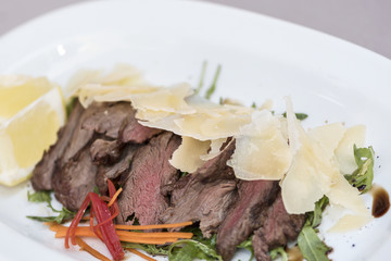 Fresh appetizer with prosciutto ham and slices of parmesan, decorated with green leaf, placed on white plate, light background, isolated