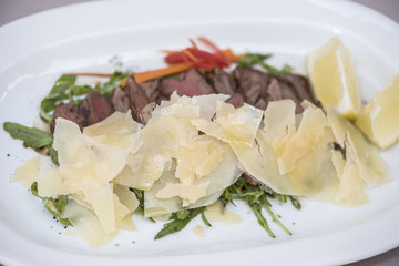 Fresh appetizer with prosciutto ham and slices of parmesan, decorated with green leaf, placed on white plate, light background, isolated