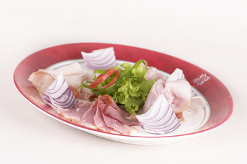 Cold cuts on plateau – different types of ham, bacon, salami, tomatoes, onion, green leafs - white and red plate, brown background