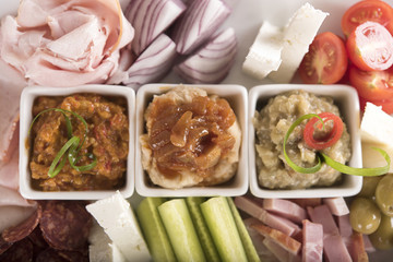 Traditional Romanian food plateau, containing different types of meat and cheese, tomatoes, onion, cucumber, olives and salads: “zacusca”, eggplant salad and beans salad, decorated with herbs, isolate