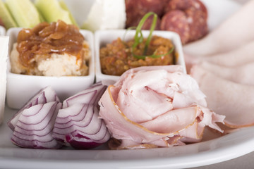 Traditional Romanian food plateau, containing different types of meat and cheese, tomatoes, onion, cucumber, olives and salads: “zacusca”, eggplant salad and beans salad, decorated with herbs, isolate