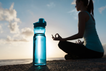 Drinking water and fitness concept. Bottle of water next to woman meditating. 