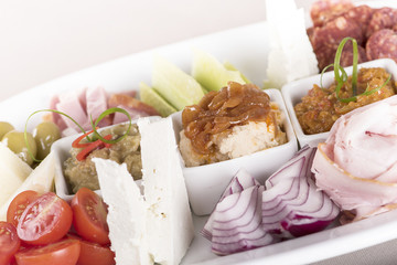 Traditional Romanian food plateau, containing different types of meat and cheese, tomatoes, onion, cucumber, olives and salads: “zacusca”, eggplant salad and beans salad, decorated with herbs, isolate