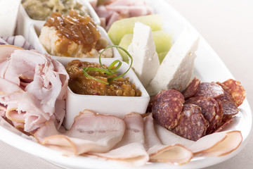 Traditional Romanian food plateau, containing different types of meat and cheese, tomatoes, onion, cucumber, olives and salads: “zacusca”, eggplant salad and beans salad, decorated with herbs, isolate