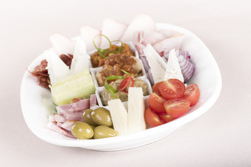 Traditional Romanian food plateau, containing different types of meat and cheese, tomatoes, onion, cucumber, olives and salads: “zacusca”, eggplant salad and beans salad, decorated with herbs, isolate
