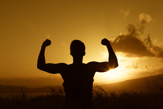 Healthy fit male flexing his arms against a beautiful sunset. 