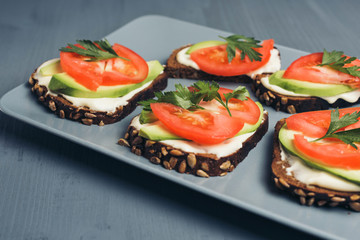 Healthy green veggie food concept. Yammy toast with cream cheese, avocado and juicy red tomato on grey plate and table.